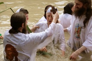 Chrisitian orthodox priests baptize a pilgrim in the waters of the Jordan River